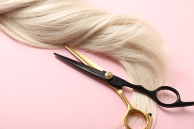 Photo of Hair strand and scissors on light pink background, closeup