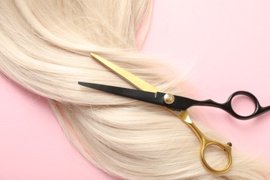 Photo of Hair strand and scissors on light pink background, closeup