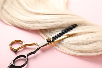 Photo of Hair strand and scissors on light pink background, closeup