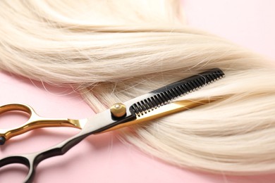 Photo of Hair strand and scissors on light pink background, closeup