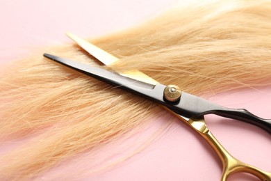 Photo of Hair strand and scissors on light pink background, closeup