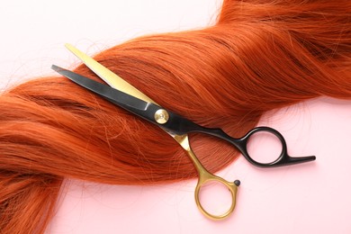 Photo of Hair strand and scissors on light pink background, top view