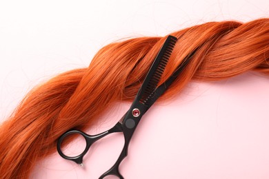 Photo of Hair strand and scissors on light pink background, top view