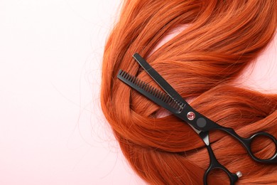 Photo of Hair strand and scissors on light pink background, top view. Space for text