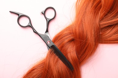 Photo of Hair strand and scissors on light pink background, top view