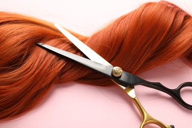 Photo of Hair strand and scissors on light pink background, closeup