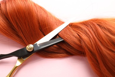 Photo of Hair strand and scissors on light pink background, closeup