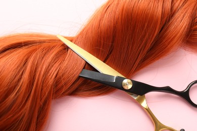 Photo of Hair strand and scissors on light pink background, closeup