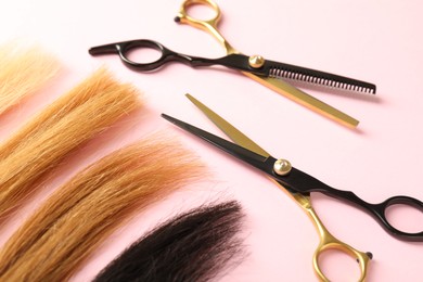 Photo of Hair strands and hairdresser's tools on light pink background, closeup