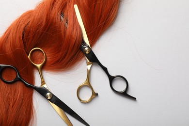 Photo of Hair strand and scissors on light background, flat lay