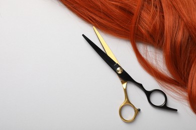 Photo of Hair strand and scissors on light background, top view. Space for text