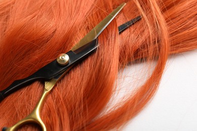 Photo of Hair strand and scissors on light background, closeup