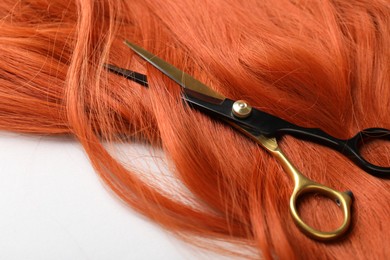Photo of Hair strand and scissors on light background, closeup