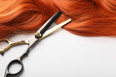 Photo of Hair strand and scissors on light background, closeup. Space for text