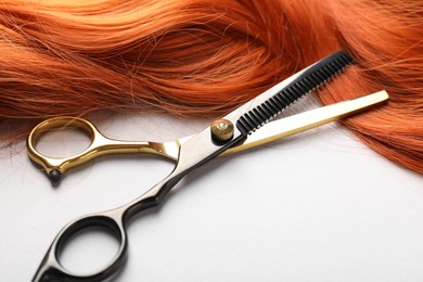 Photo of Hair strand and scissors on light background, closeup