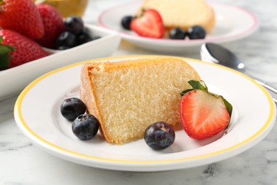 Photo of Pieces of tasty bundt cake with berries on white marble table, closeup
