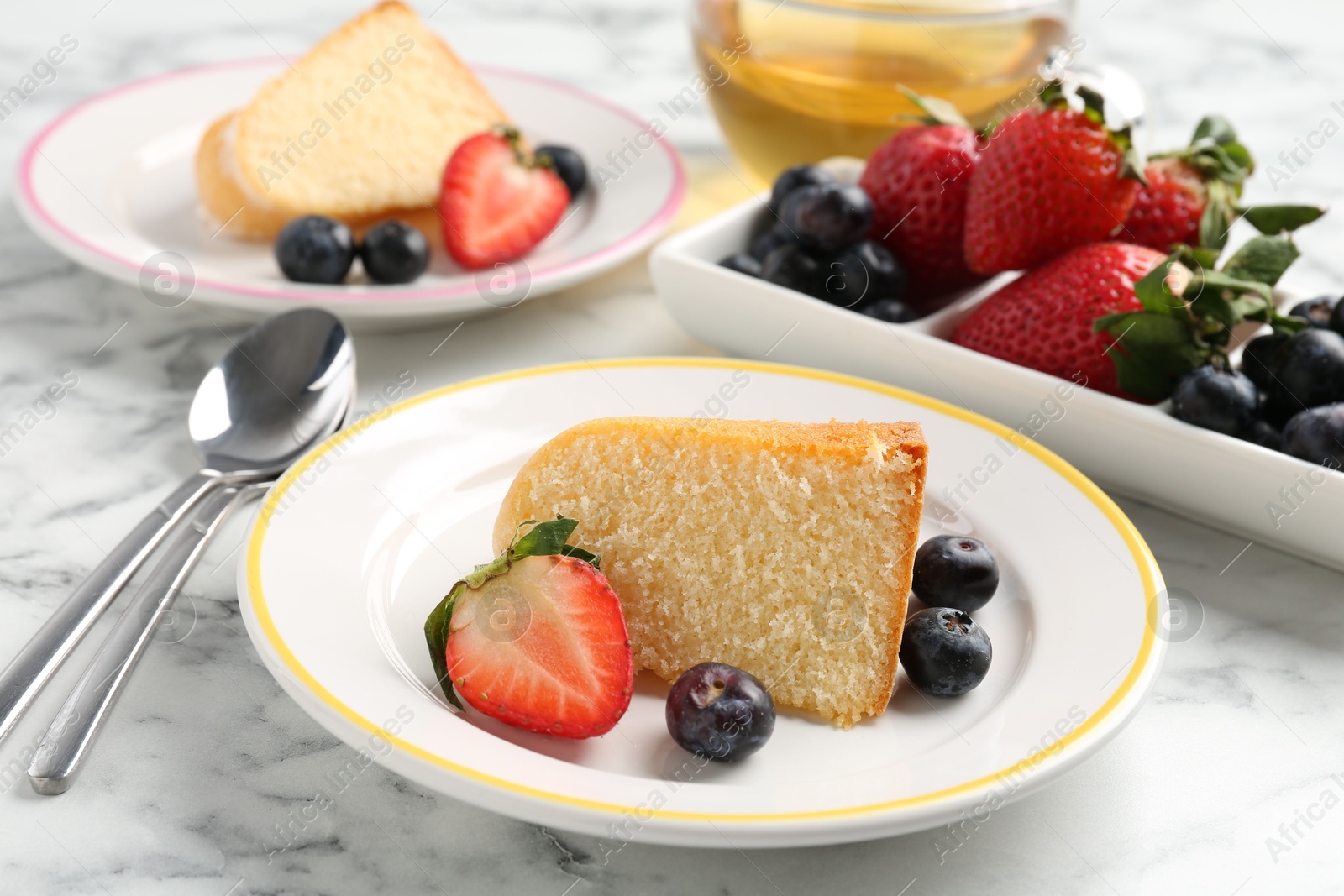 Pieces of tasty bundt cake with berries and tea on white marble table, closeup Photo of Pieces of tasty bundt cake with berries and tea on white marble table, closeup
