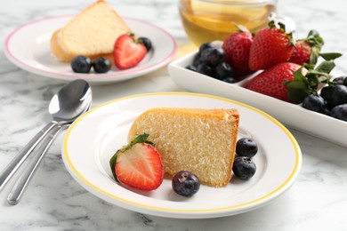Photo of Pieces of tasty bundt cake with berries and tea on white marble table, closeup