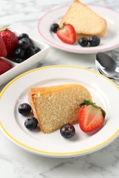 Photo of Pieces of tasty bundt cake with berries on white marble table, closeup