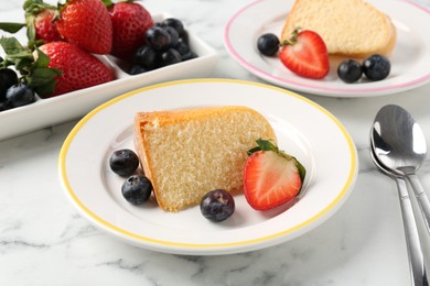 Photo of Pieces of tasty bundt cake with berries on white marble table, closeup
