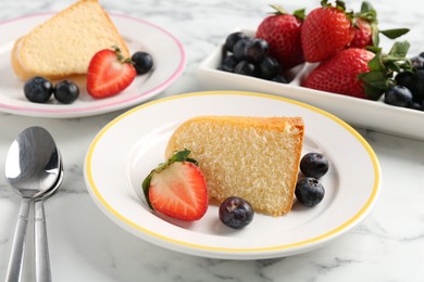 Photo of Pieces of tasty bundt cake with berries on white marble table, closeup