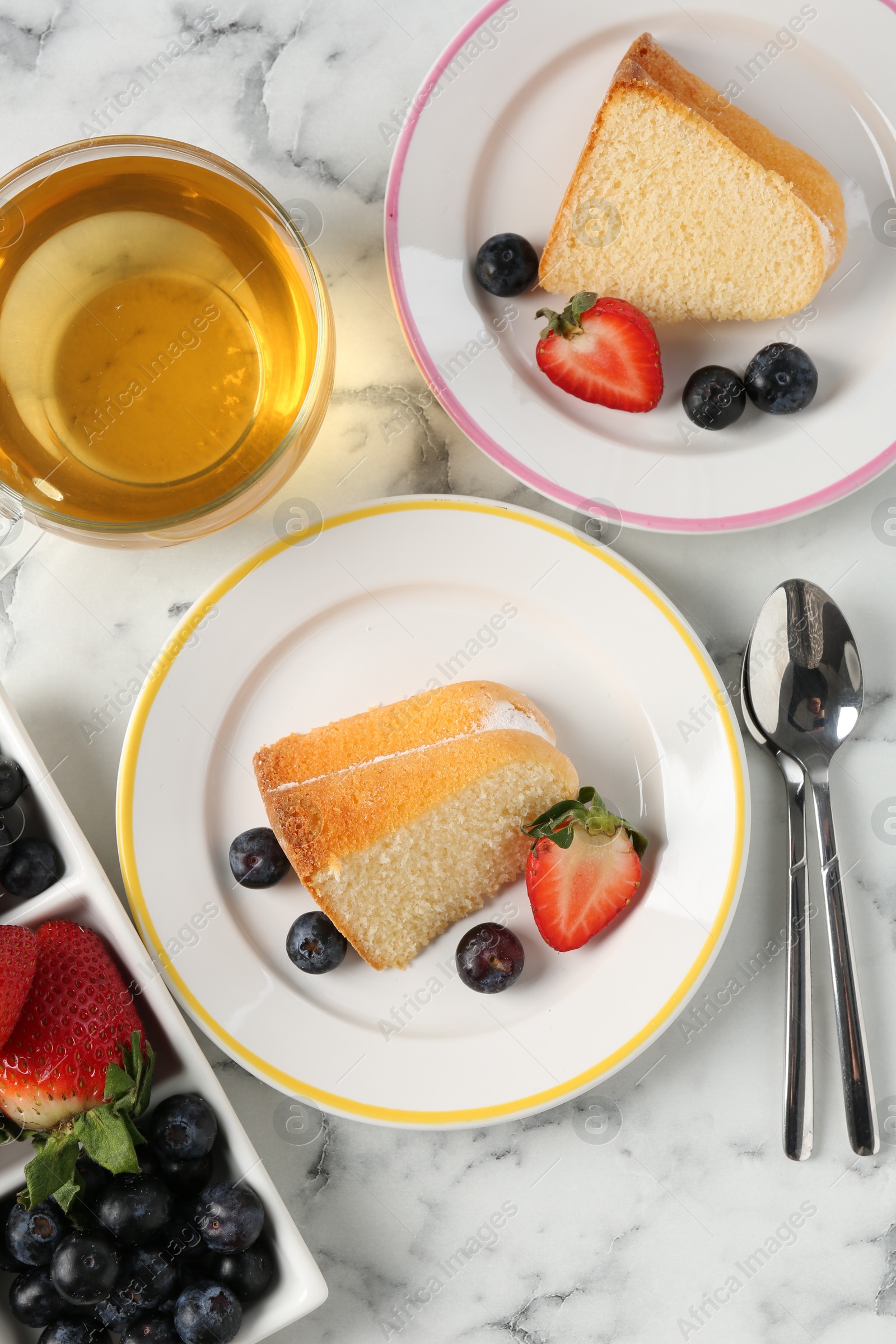 Pieces of tasty bundt cake with berries and tea on white marble table, flat lay Photo of Pieces of tasty bundt cake with berries and tea on white marble table, flat lay