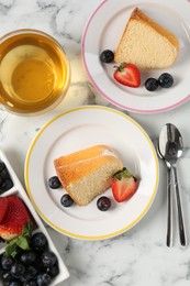 Photo of Pieces of tasty bundt cake with berries and tea on white marble table, flat lay