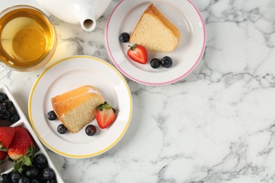 Photo of Pieces of tasty bundt cake with berries and tea on white marble table, flat lay. Space for text