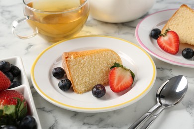 Photo of Pieces of tasty bundt cake with berries and tea on white marble table, closeup