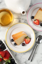 Photo of Pieces of tasty bundt cake with berries and tea on white marble table, flat lay