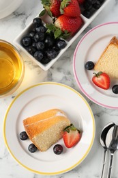 Photo of Pieces of tasty bundt cake with berries and tea on white marble table, flat lay