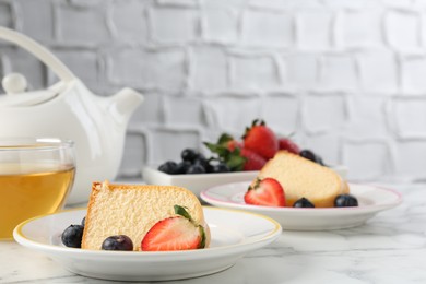 Photo of Pieces of tasty bundt cake with berries and tea on white marble table, closeup