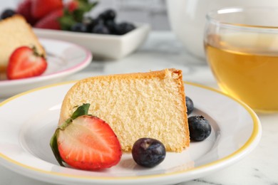 Photo of Piece of tasty bundt cake with berries and tea on white marble table, closeup