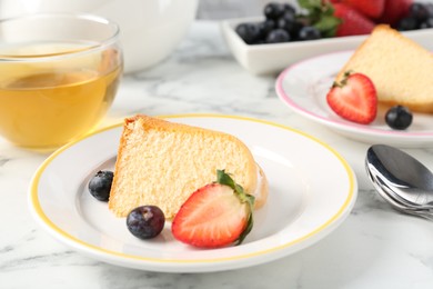Photo of Pieces of tasty bundt cake with berries and tea on white marble table, closeup