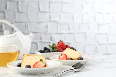 Photo of Pieces of tasty bundt cake with berries and tea on white marble table, closeup