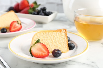 Photo of Pieces of tasty bundt cake with berries and tea on white marble table, closeup