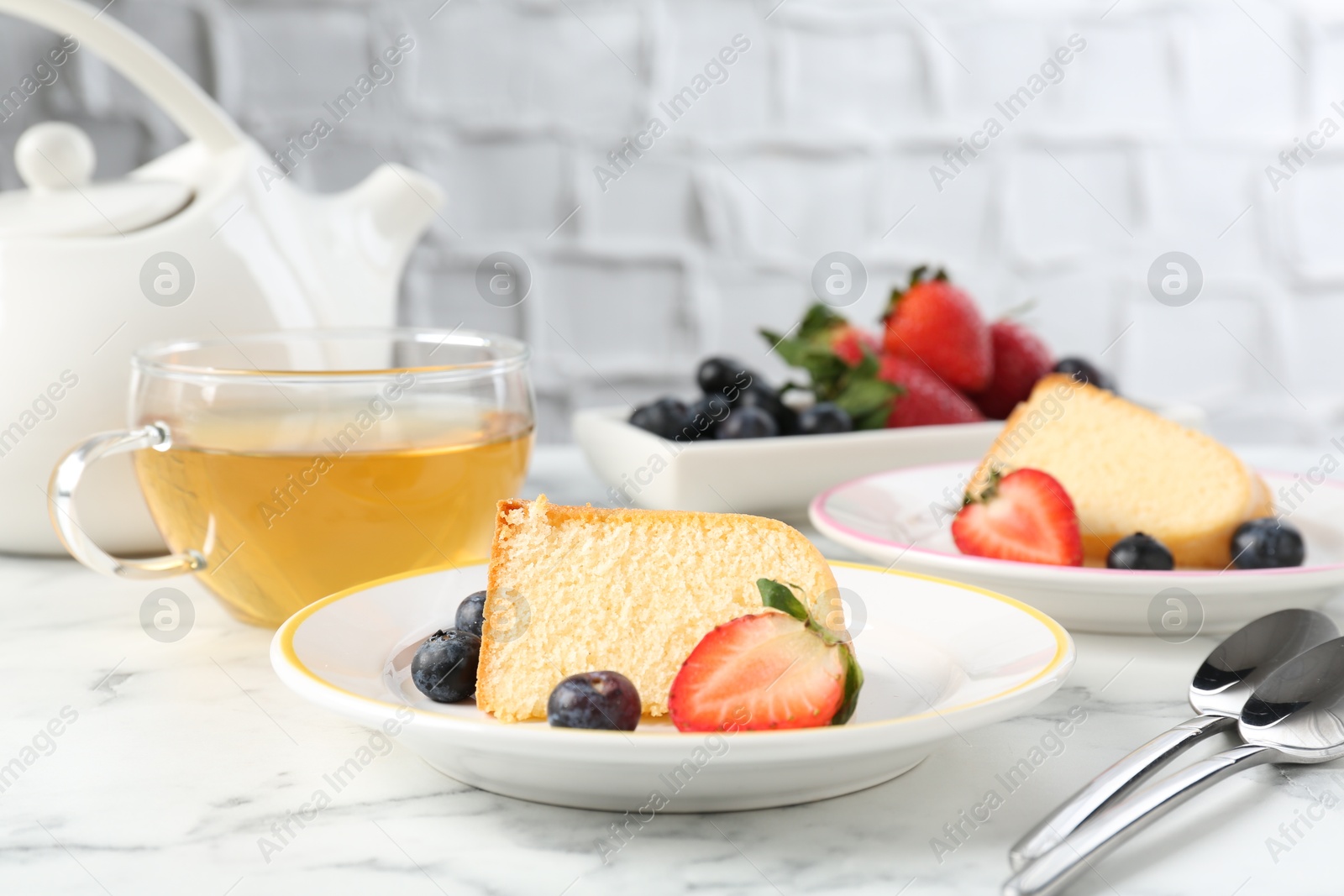 Pieces of tasty bundt cake with berries and tea on white marble table, closeup Photo of Pieces of tasty bundt cake with berries and tea on white marble table, closeup