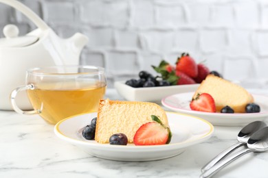 Photo of Pieces of tasty bundt cake with berries and tea on white marble table, closeup