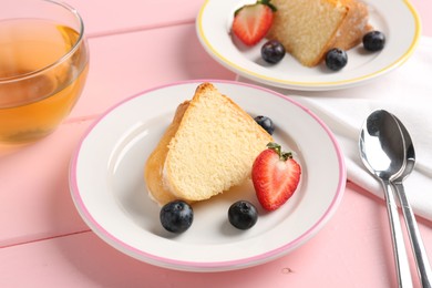 Photo of Pieces of tasty bundt cake with berries and tea on pink wooden table, closeup