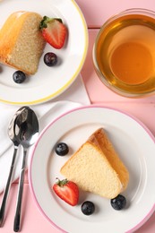Photo of Pieces of tasty bundt cake with berries and tea on pink wooden table, flat lay
