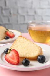 Photo of Piece of tasty bundt cake with berries and tea on pink table, closeup