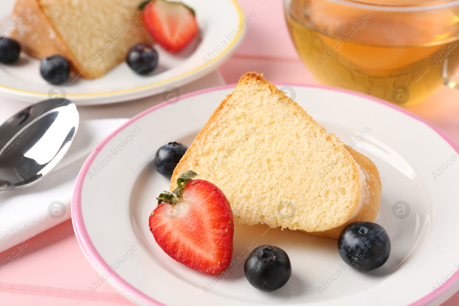 Photo of Pieces of tasty bundt cake with berries and tea on pink table, closeup