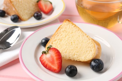 Photo of Pieces of tasty bundt cake with berries and tea on pink table, closeup