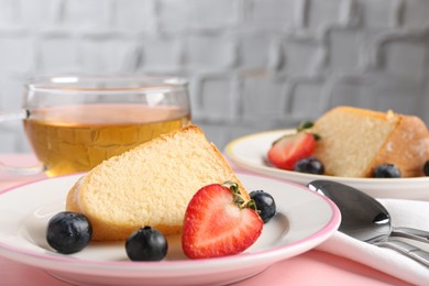 Photo of Pieces of tasty bundt cake with berries and tea on pink table, closeup