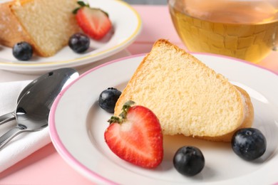 Photo of Pieces of tasty bundt cake with berries and tea on pink table, closeup