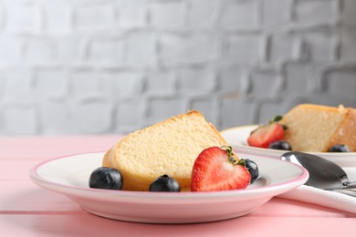 Photo of Pieces of tasty bundt cake with berries on pink wooden table, closeup