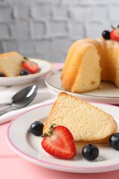 Photo of Pieces of tasty bundt cake with berries on pink wooden table, closeup