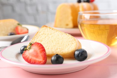 Photo of Tasty bundt cake with berries and tea on pink wooden table, closeup