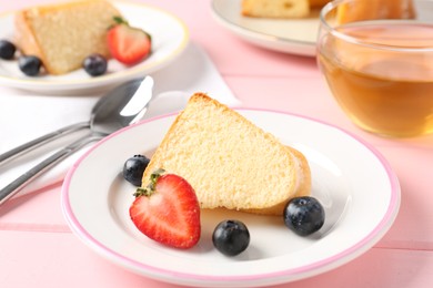Photo of Tasty bundt cake with berries and tea on pink wooden table, closeup