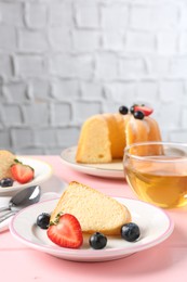 Photo of Tasty bundt cake with berries and tea on pink wooden table, closeup
